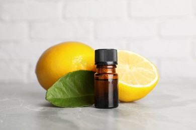 Photo of Bottle of essential oil with lemons and leaf on grey marble table against white brick wall, closeup