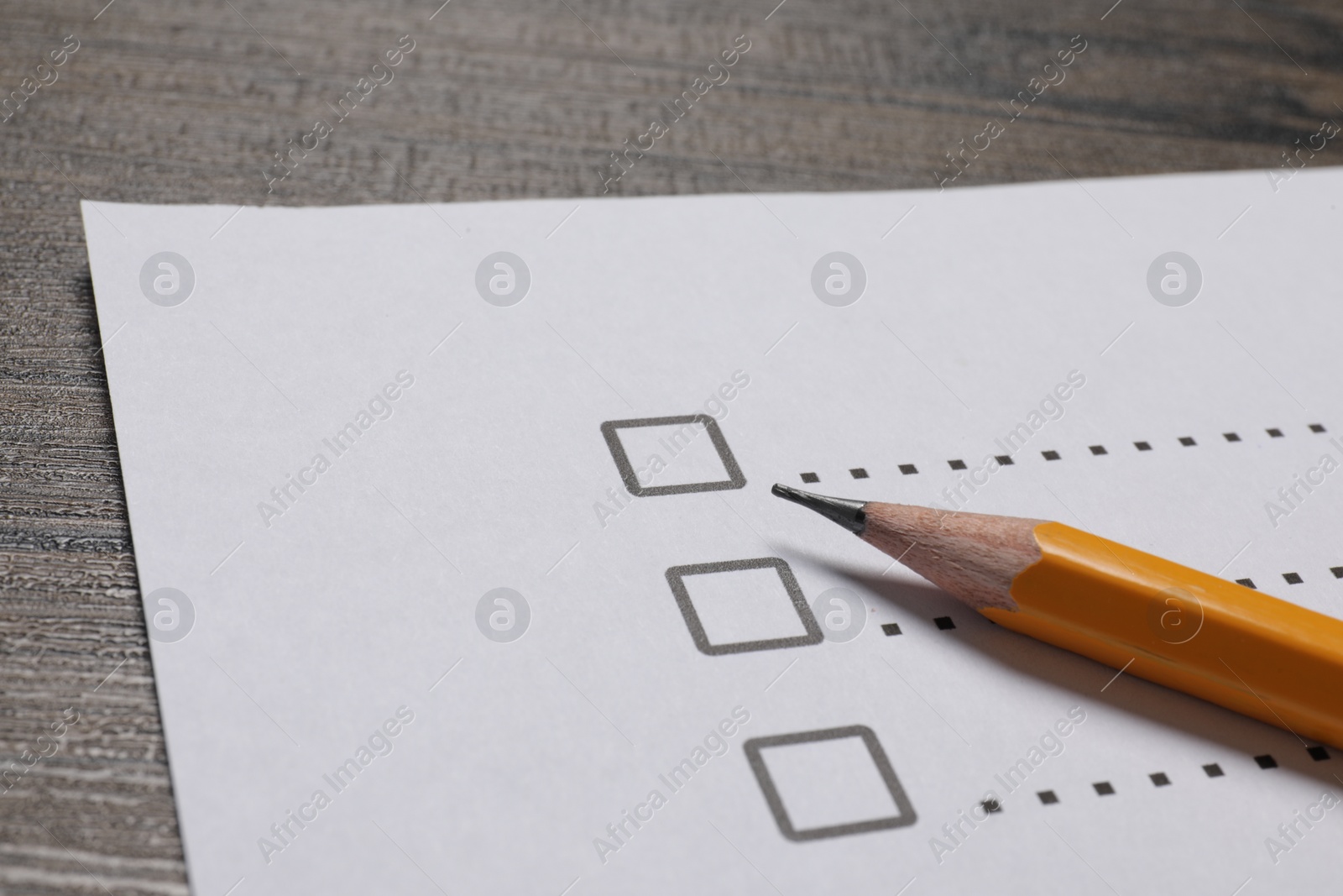 Photo of Paper sheet with checkboxes and pencil on wooden table, closeup. Checklist