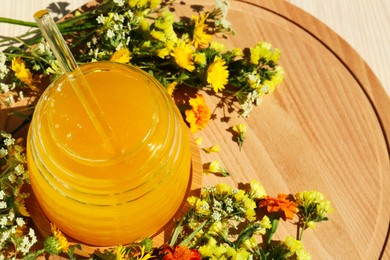 Photo of Delicious fresh honey in glass jar and beautiful flowers on wooden board. Space for text