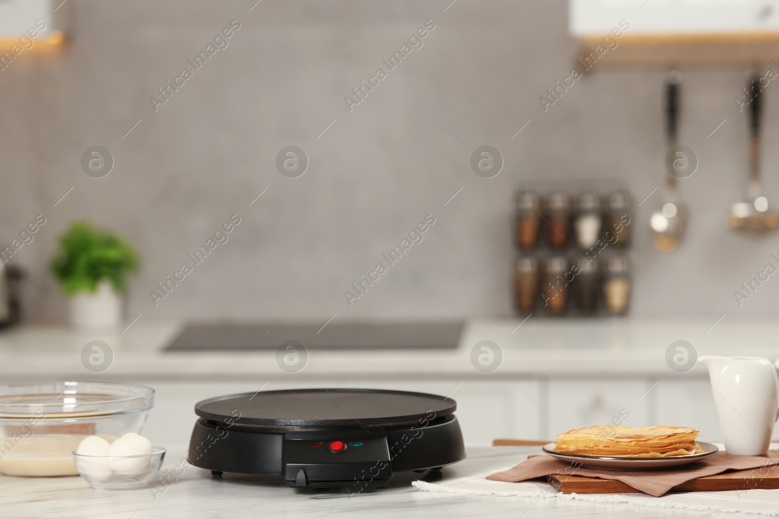 Photo of Electric crepe maker and ingredients on white marble table in kitchen