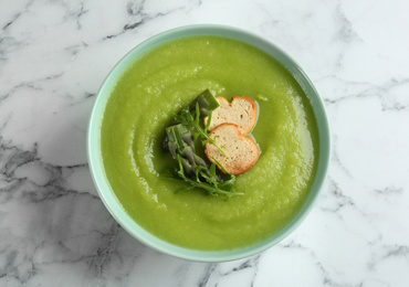 Photo of Delicious asparagus soup in bowl on white marble table, top view