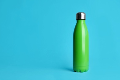 Stylish thermo bottle on light blue background, space for text