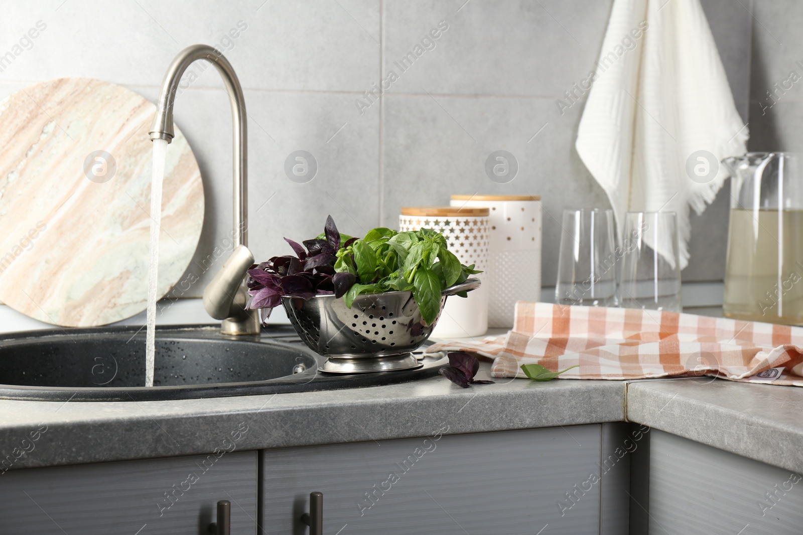 Photo of Metal colander with different fresh basil leaves on grey countertop near sink