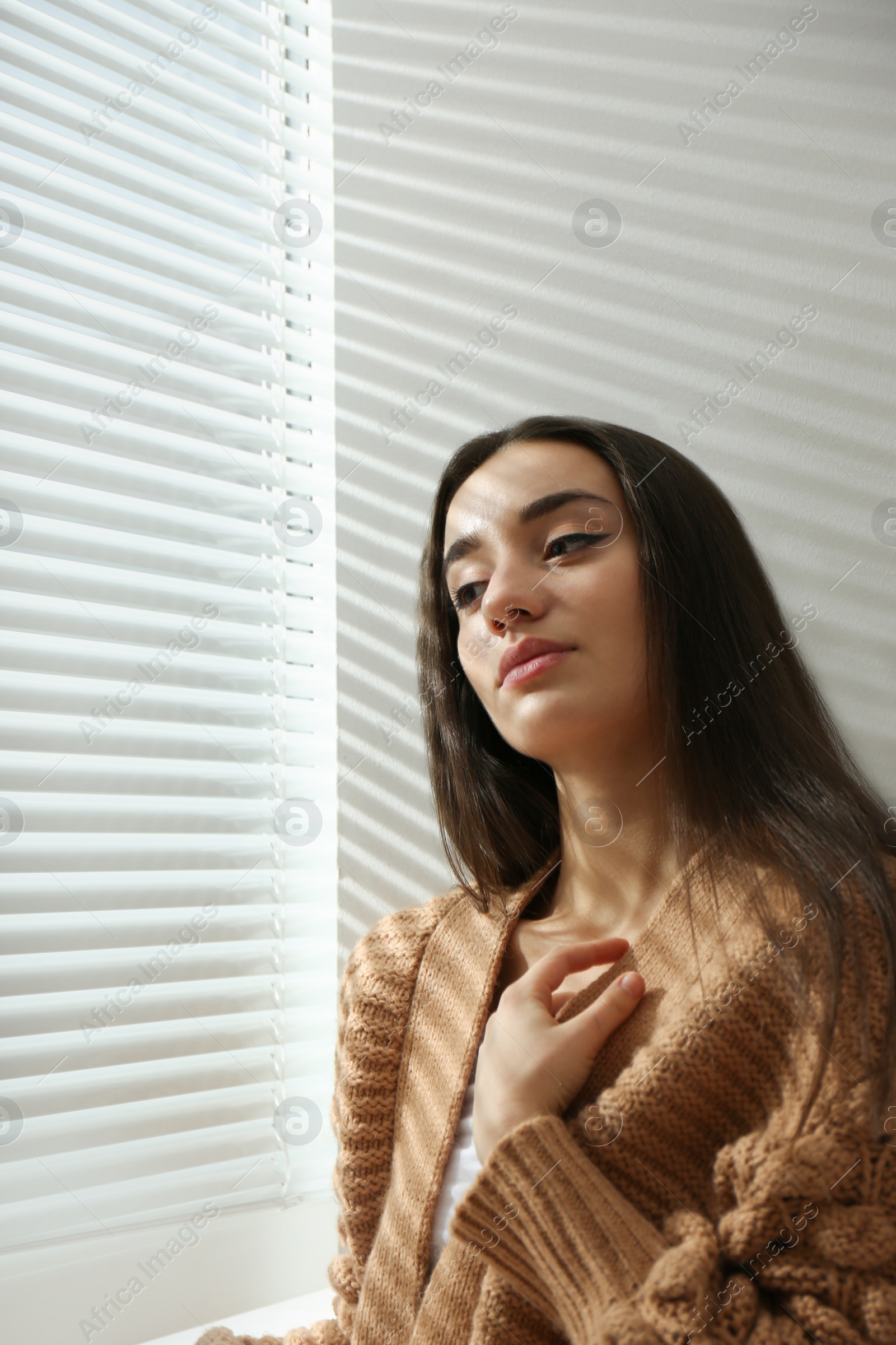 Photo of Young woman near window with Venetian blinds