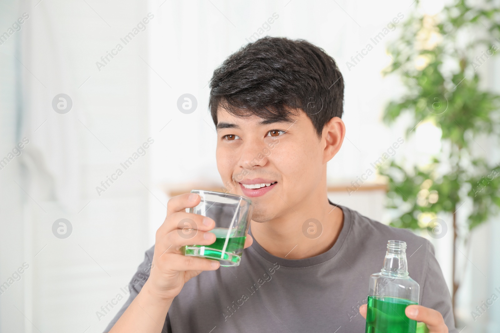 Photo of Man holding bottle and glass with mouthwash in bathroom. Teeth care