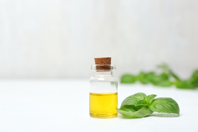 Photo of Glass bottle with oil and basil leaves on table. Space for text