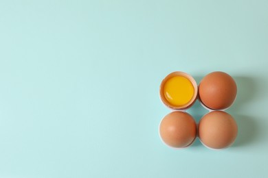 Cracked and whole chicken eggs on light blue background, flat lay. Space for text
