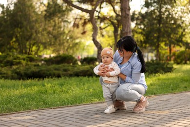 Mother teaching her baby how to walk outdoors. Space for text