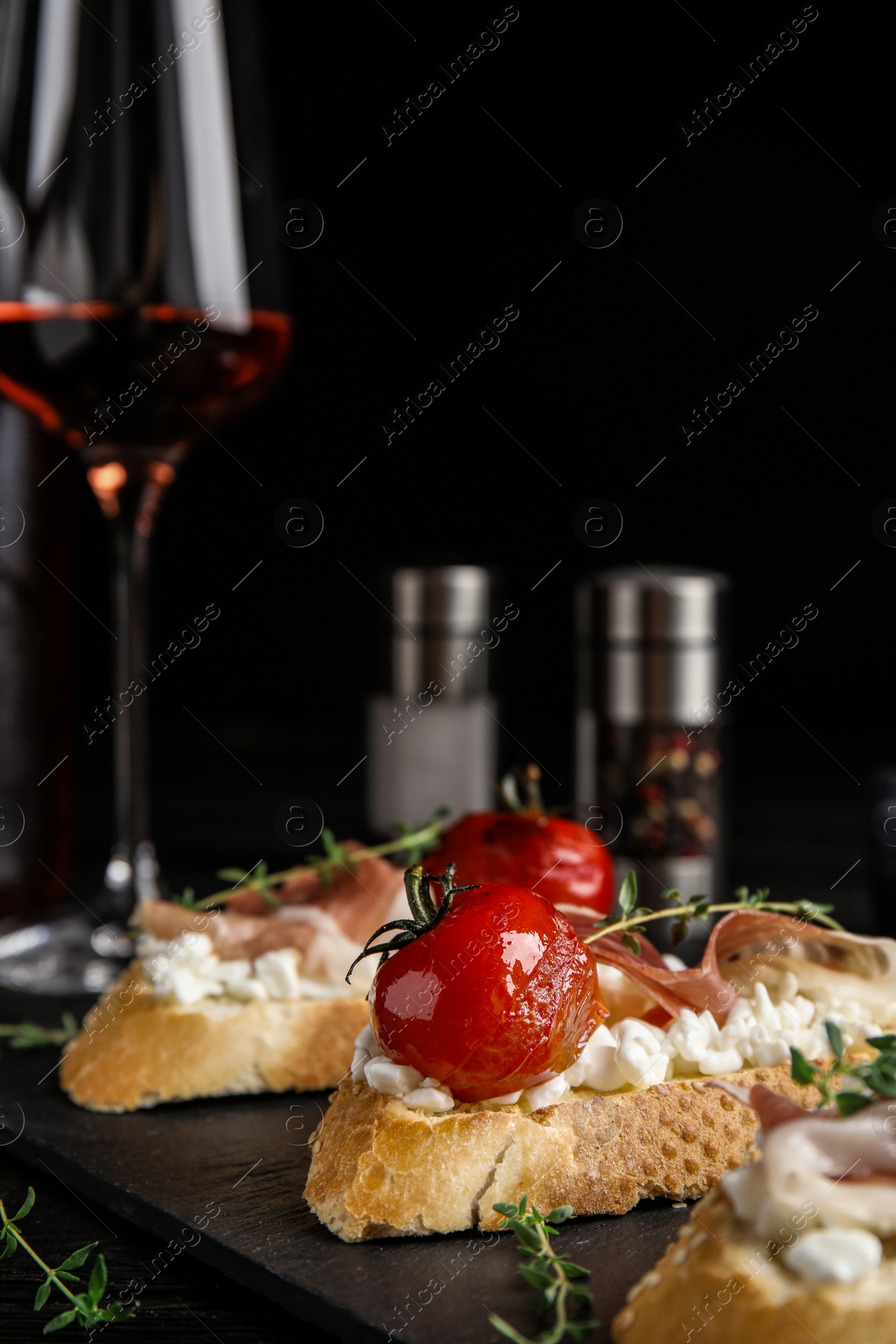 Photo of Slate plate of delicious bruschettas with prosciutto on black wooden table