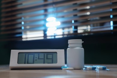 Photo of Digital alarm clock and pills on table indoors. Insomnia treatment