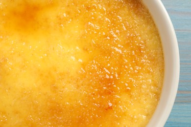 Photo of Delicious creme brulee in ceramic ramekin on light blue wooden table, closeup