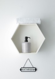 Stylish hexagon shaped shelf with towel and soap dispenser above Bathroom sign on white wall. Interior element