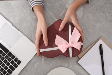 Woman with gift box at light grey marble table, flat lay. Valentine's day celebration