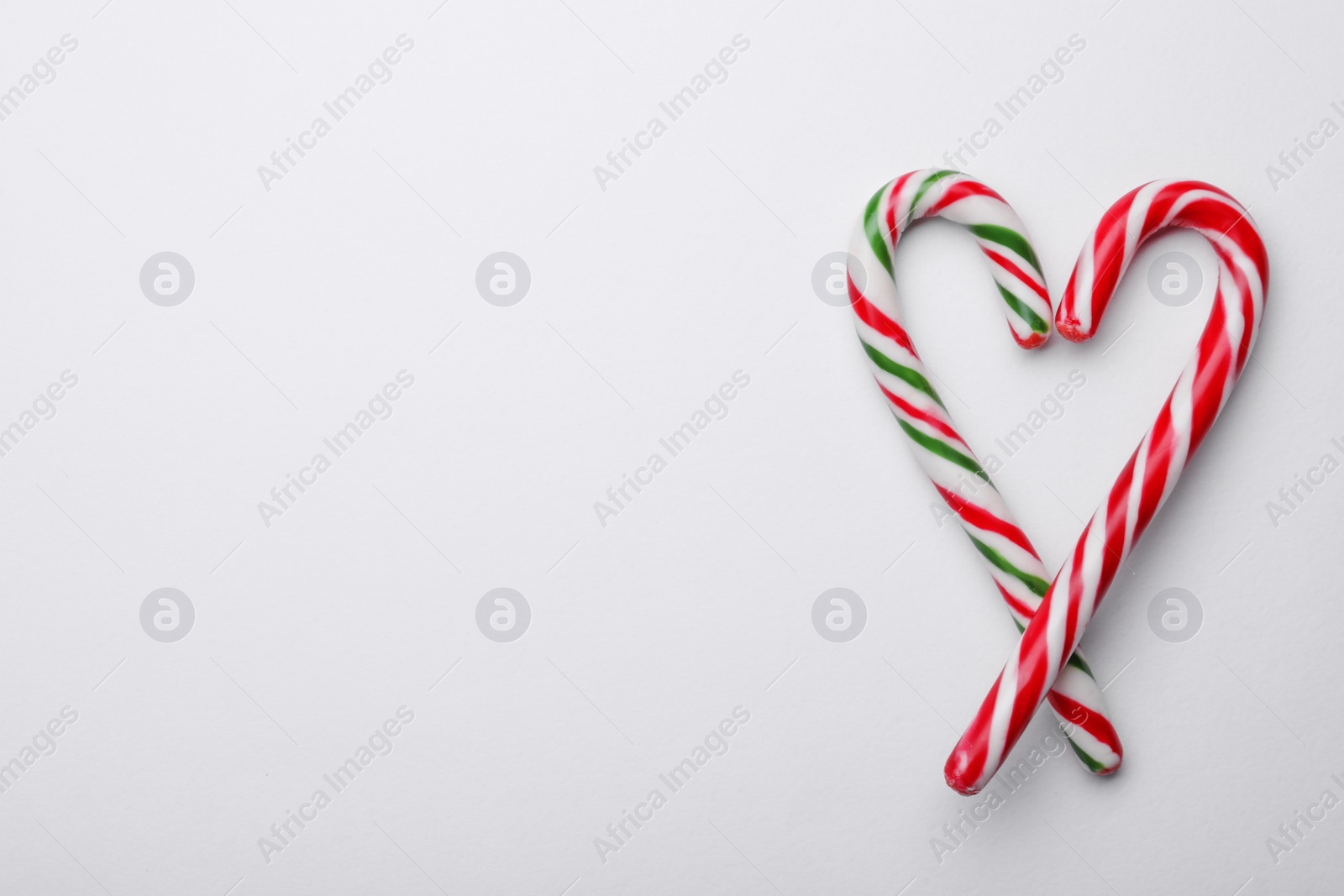 Photo of Heart made of sweet Christmas candy canes on white background, top view. Space for text