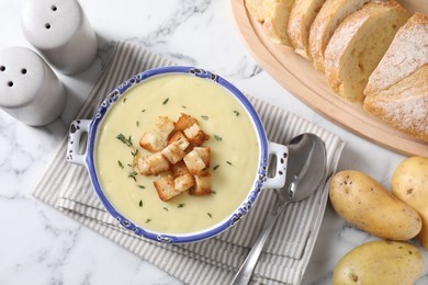 Tasty potato soup with croutons and rosemary in ceramic pot served on white marble table, flat lay