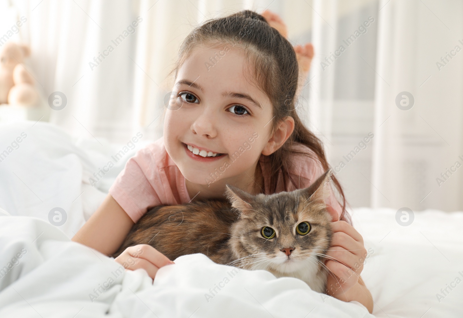 Photo of Cute little girl with cat lying on bed at home. First pet