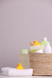 Photo of Wicker basket with baby cosmetic products, bath accessories and rubber ducks on white table against grey background