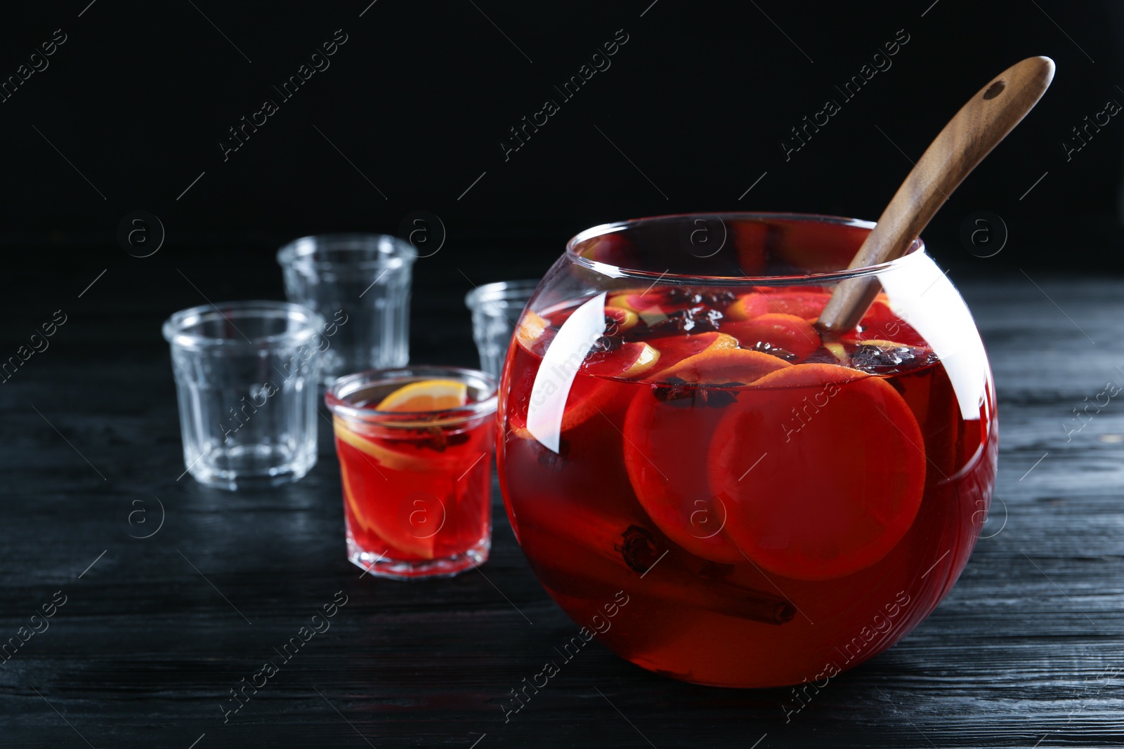 Photo of Glasses near bowl of delicious aromatic punch drink on black wooden table