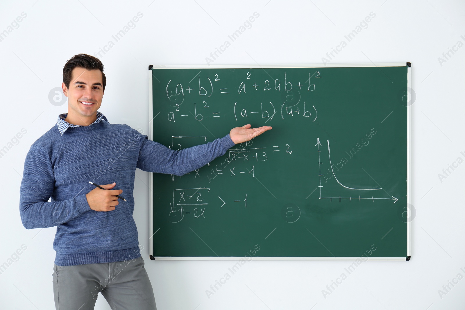 Photo of Young teacher explaining math formulas written on chalkboard in classroom