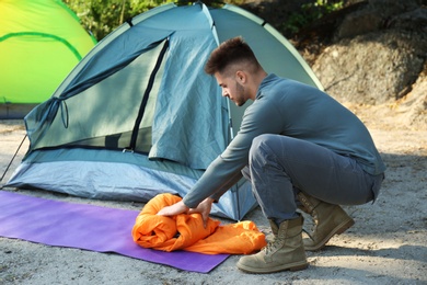 Photo of Young man with sleeping bag near tent outdoors