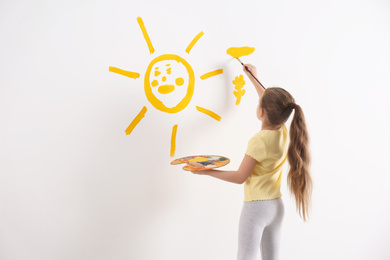 Little child painting sun on white wall indoors