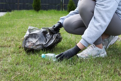 Photo of Woman with trash bag picking up plastic bottle outdoors, closeup. Recycling concept