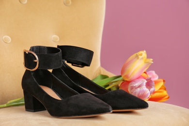 Pair of female shoes and flowers on chair against color background