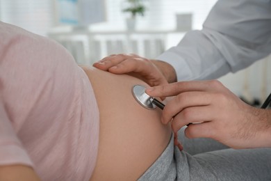 Doctor examining pregnant woman with stethoscope in clinic, closeup