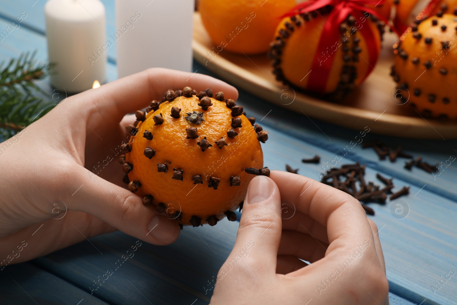 Photo of Woman decorating fresh tangerine with cloves at light blue wooden table, closeup