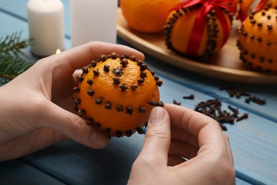 Woman decorating fresh tangerine with cloves at light blue wooden table, closeup
