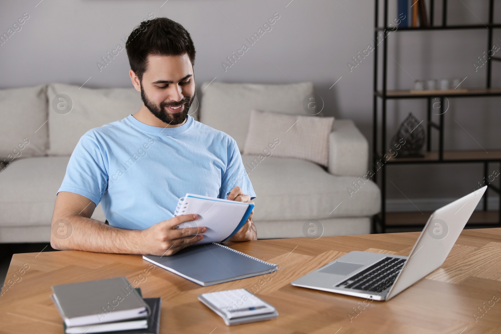 Photo of Young man writing down notes during webinar at table in room