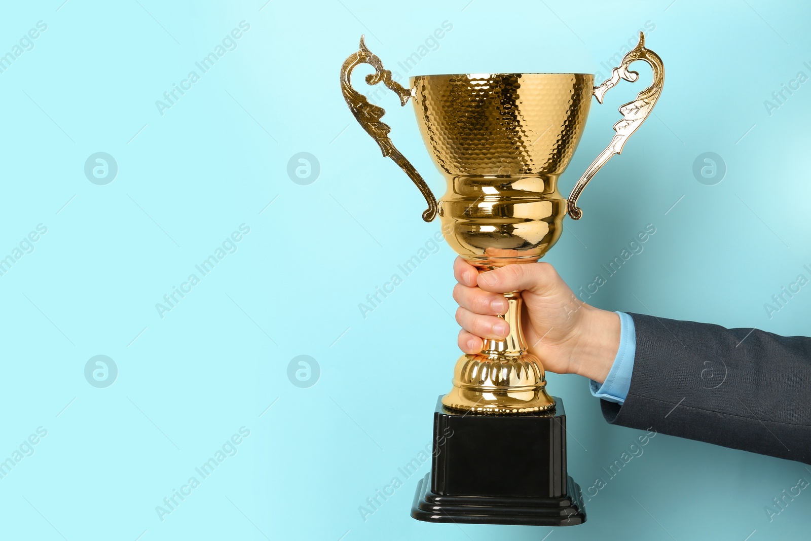 Photo of Man holding golden trophy cup on color background, closeup. Space for text