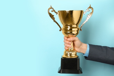 Man holding golden trophy cup on color background, closeup. Space for text