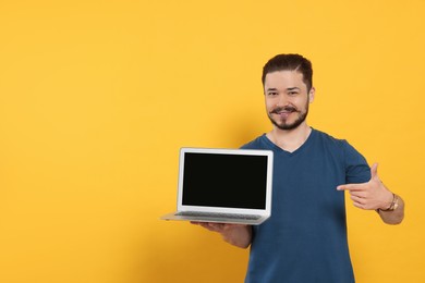 Photo of Emotional man pointing at laptop on orange background. Space for text