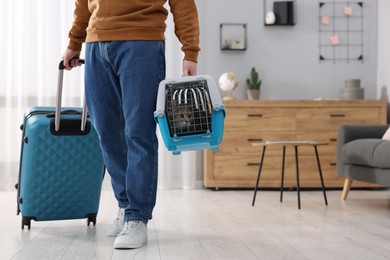 Photo of Travel with pet. Man holding carrier with cute cat and suitcase at home, closeup. Space for text