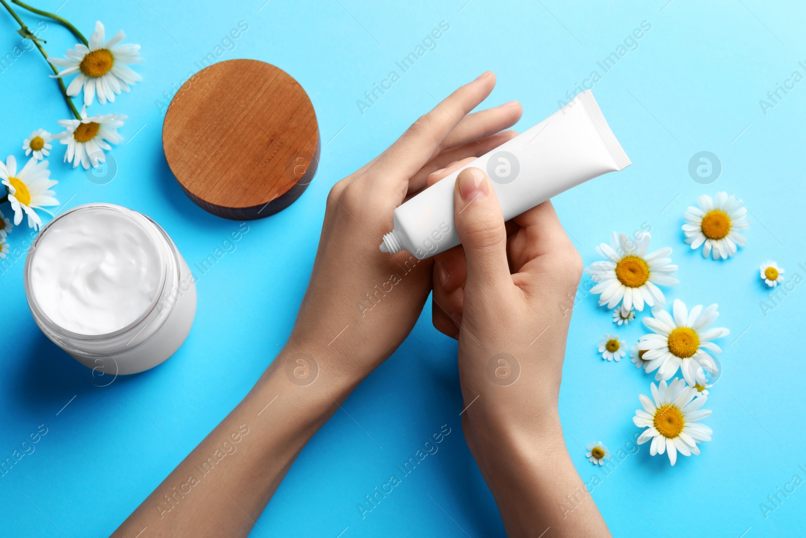 Photo of Woman applying hand cream on light blue background, top view