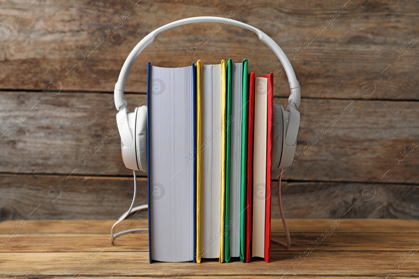 Photo of Modern headphones with hardcover books on wooden table