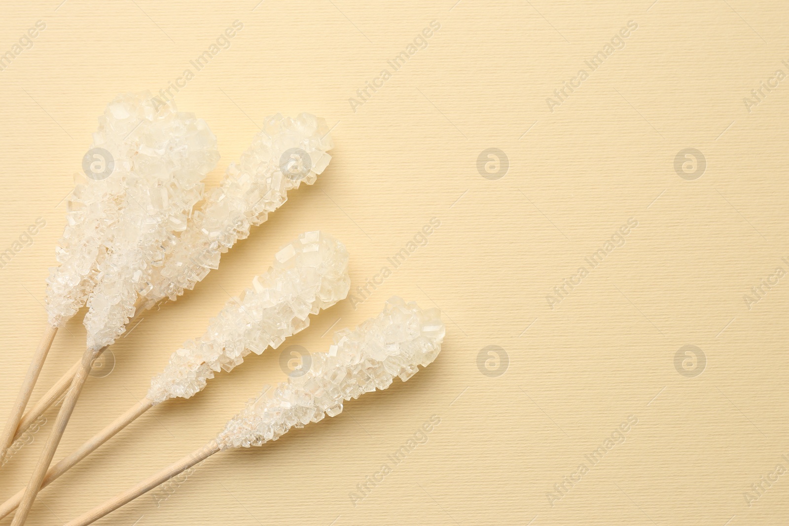 Photo of Wooden sticks with sugar crystals and space for text on beige background, flat lay. Tasty rock candies