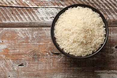 Photo of Raw basmati rice in bowl on wooden table, top view. Space for text