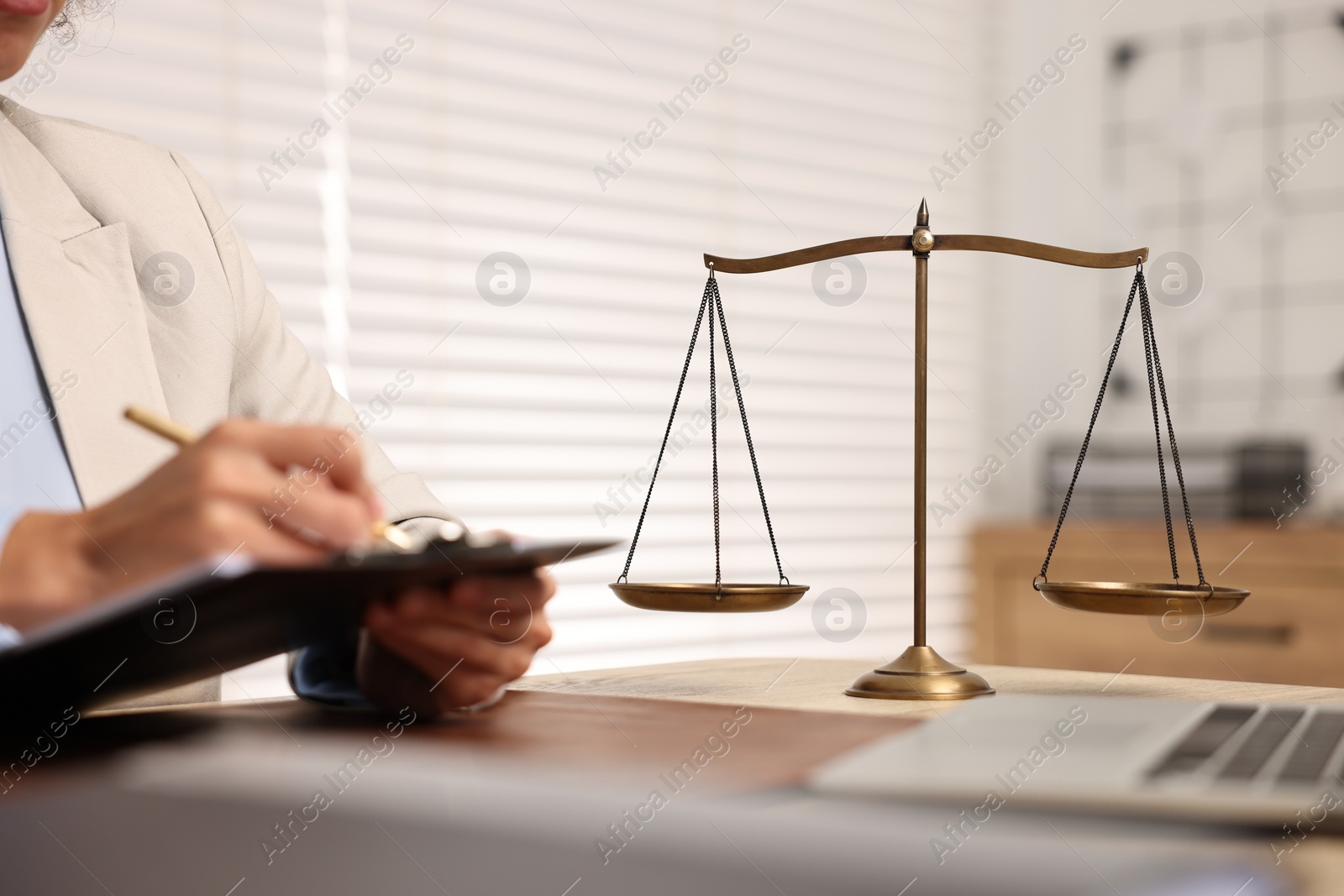 Photo of Notary with clipboard writing notes at workplace in office, focus on scales of justice