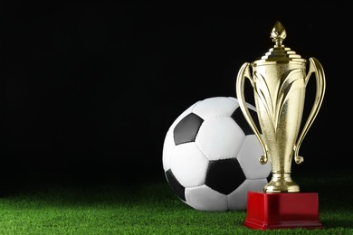 Golden trophy cup and soccer ball on football field. Space for text