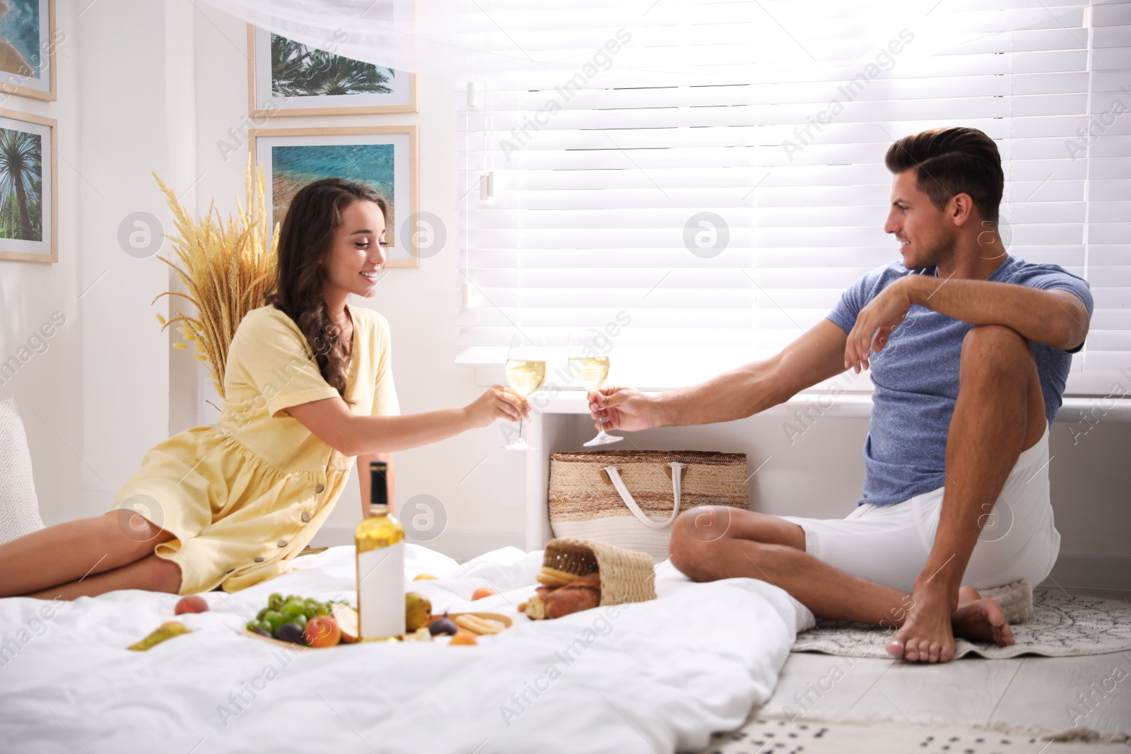 Photo of Happy couple with wine and tasty food imitating picnic at home