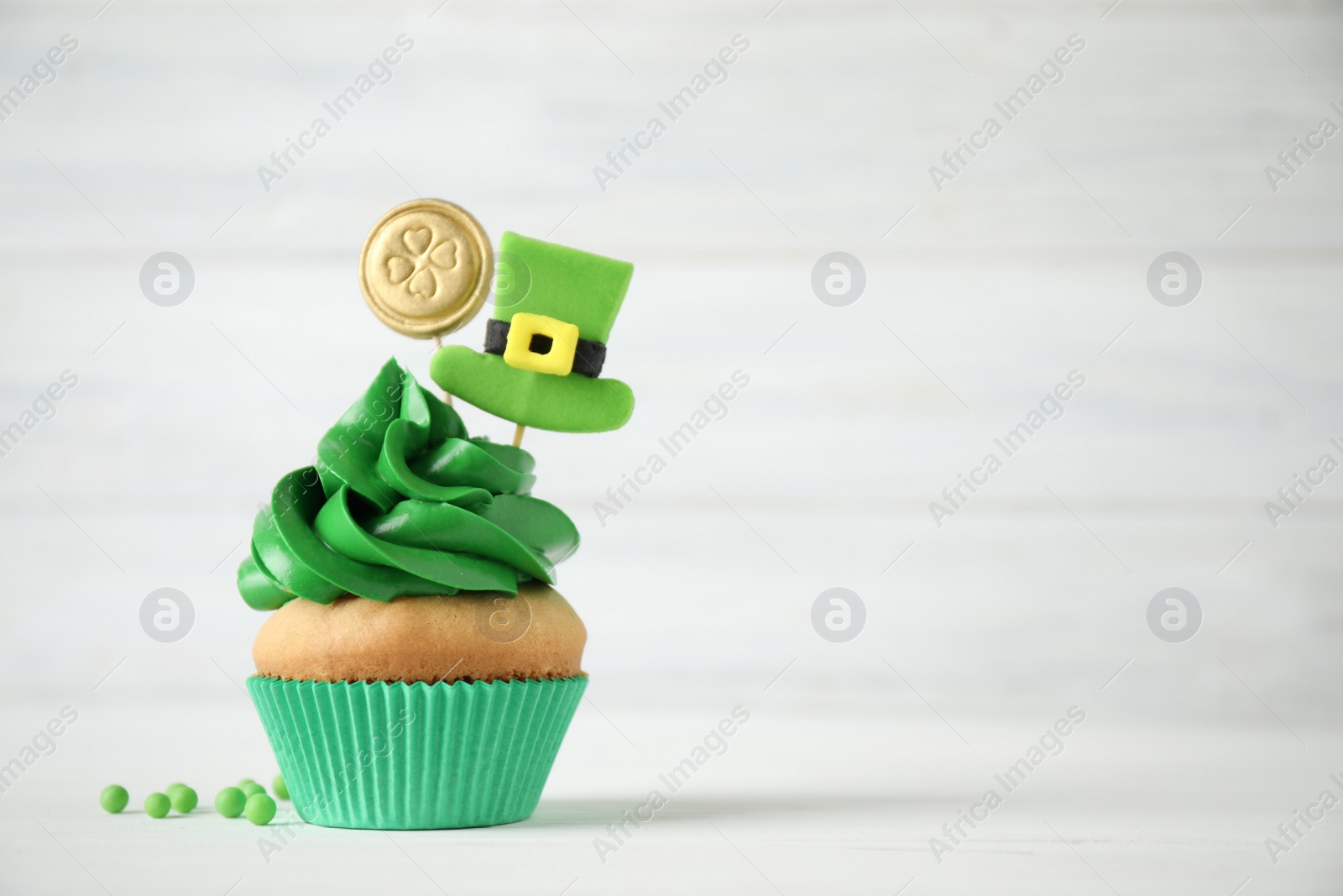 Photo of Decorated cupcake on white wooden table, space for text. St. Patrick's Day celebration