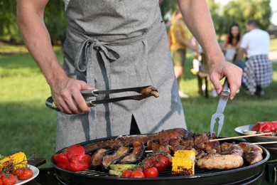 Photo of Man cooking meat and vegetables on barbecue grill outdoors, closeup