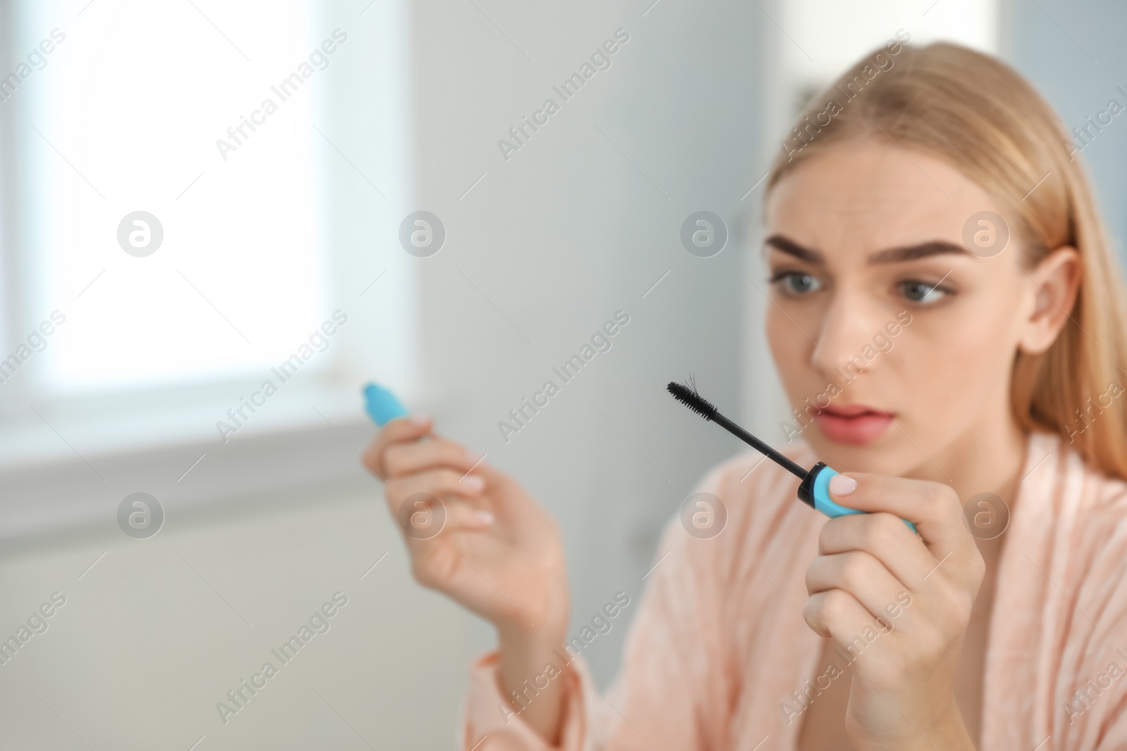 Photo of Young woman holding mascara brush with fallen eyelashes indoors