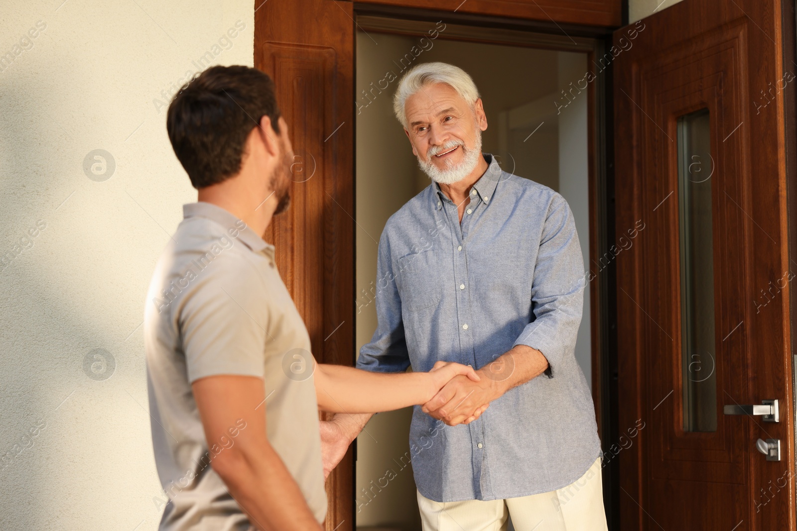 Photo of Friendly relationship with neighbours. Happy men shaking hands near house outdoors