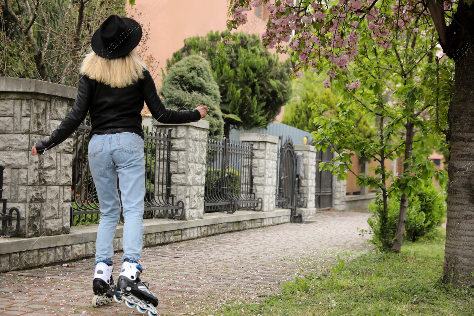 Photo of Young woman roller skating on spring day, back view