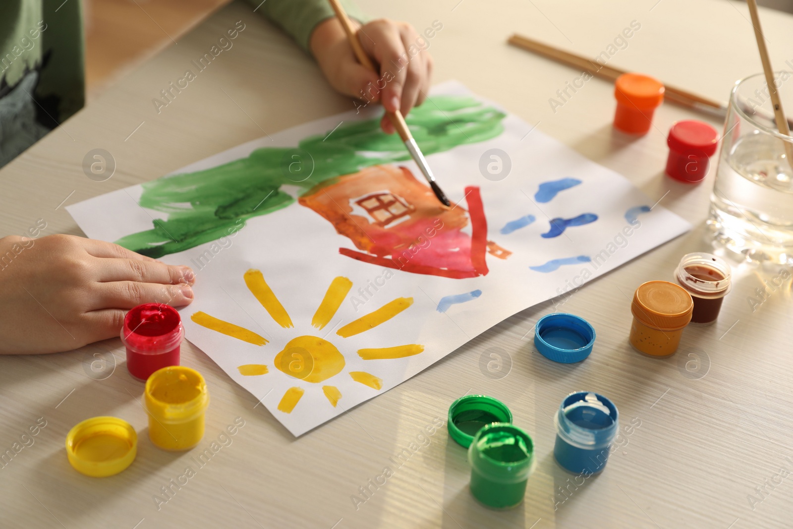 Photo of Little boy drawing picture with brush at wooden table, closeup. Child`s art