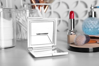Photo of Stylish pocket mirror and cosmetic products on white table