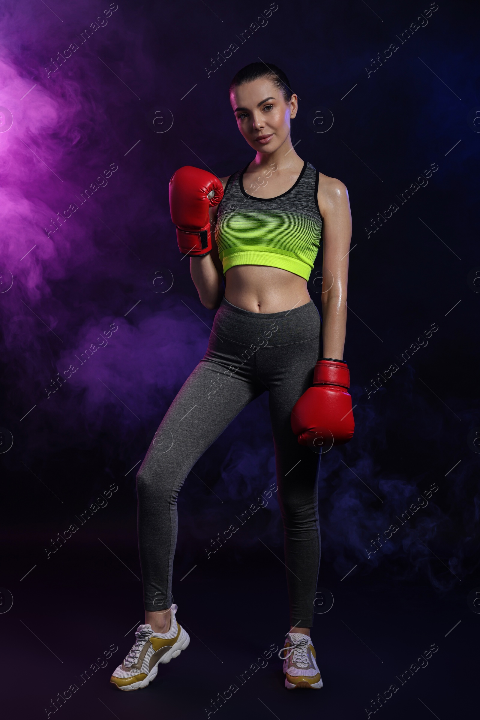 Photo of Beautiful woman wearing boxing gloves in color lights and smoke on black background